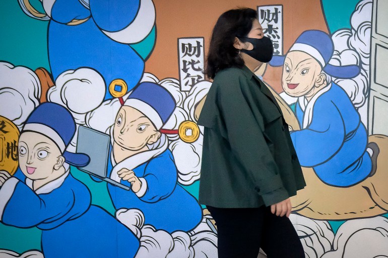 A woman wearing a face mask walks past a mural of health workers in blue medical gowns in Beijing.