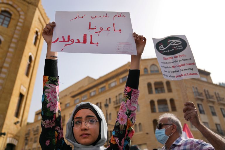 A protester holds a sign in Arabic that reads: "Our rulers sold us in dollars," during a protest against a new draft law on capital controls that would limit how much bank depositors can withdraw from their savings, outside the parliament building, in downtown Beirut, Lebanon, Tuesday, April 26, 2022. Lebanon is in the grip of a severe economic crisis that was described by the World Bank as one of the worst the world has witnessed since the 1850s.