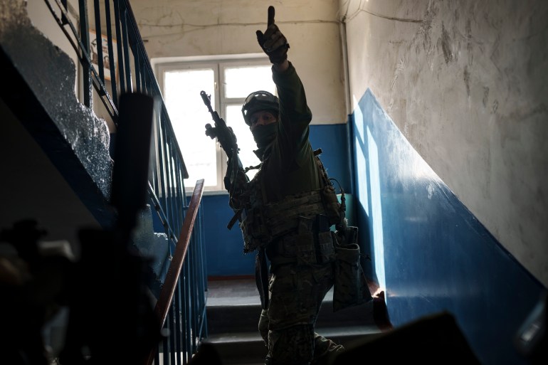 Soldier walking up stairs with a weapon in his right hand and pointing up with his left.