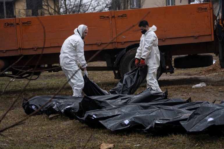 Cemetery workers carry a corpse of a man from a mass grave, to be identified in a morgue. Bucha, outside Kyiv.