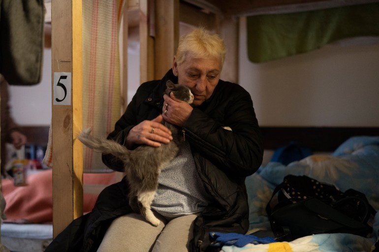 A woman pets her cat as she sits on a bed in a restaurant that was transformed into a shelter for those fleeing the war in Dnipro, Ukraine.