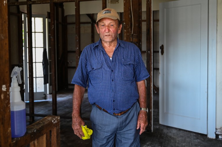 Toby Bell, in blue shirt and jeans, stands in his flood ravaged house