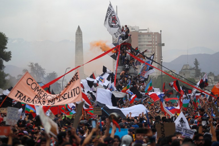 Protesters wave Chilean flags and climb the monument to General Baquedano