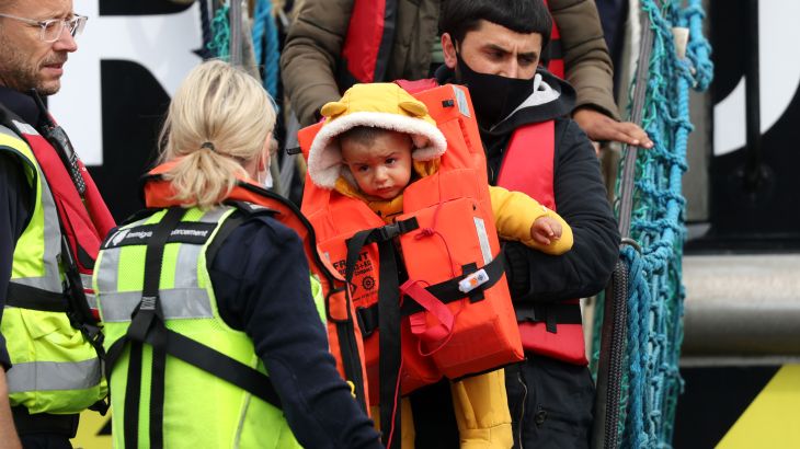 A man carries a child in a life jacket off a boat.