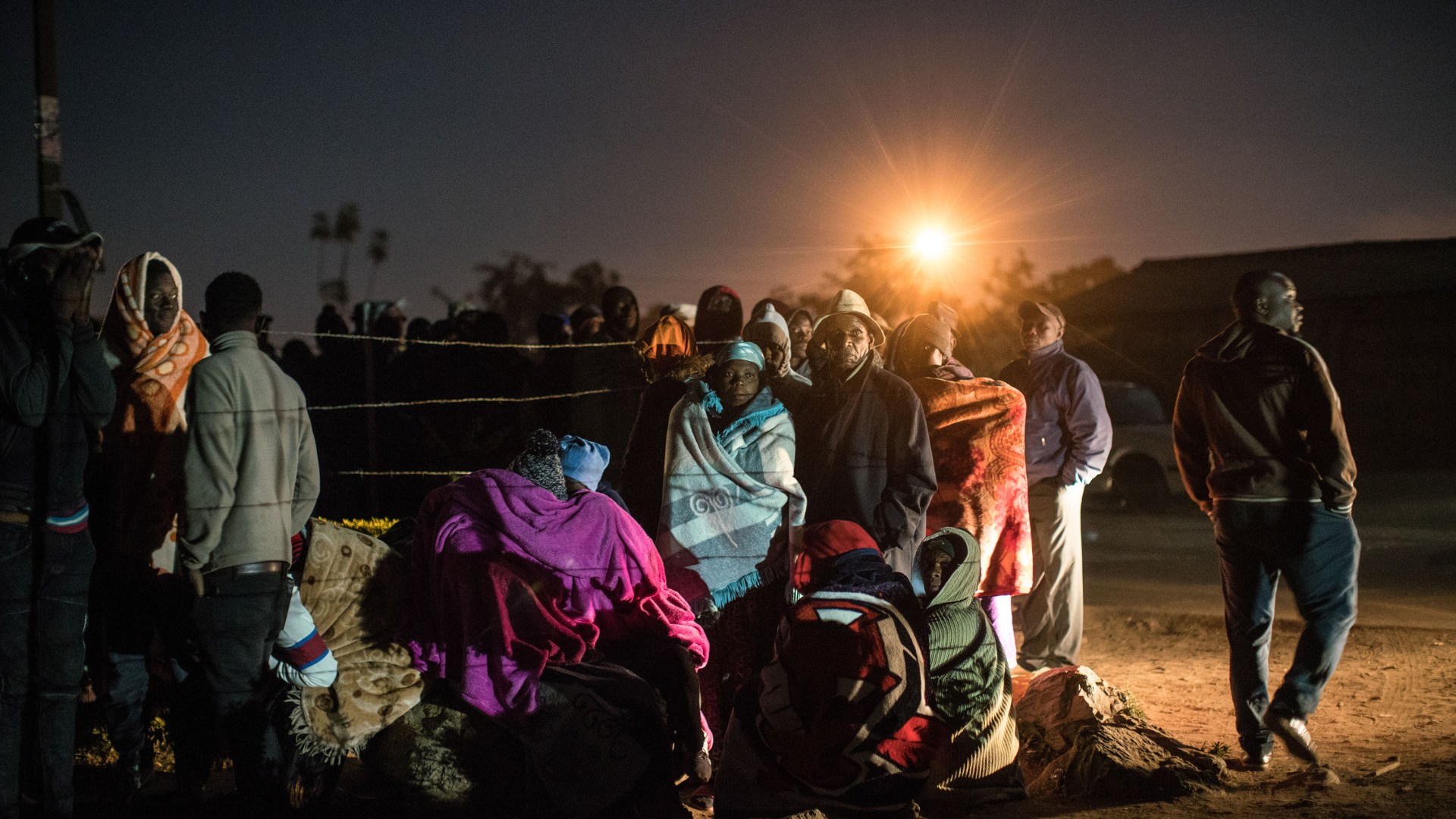 A photo of people queuing in the dark with the sun rising.