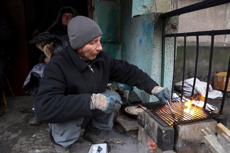 Resident in Mariupol prepares to cook at an entrance of a building damaged during fighting.