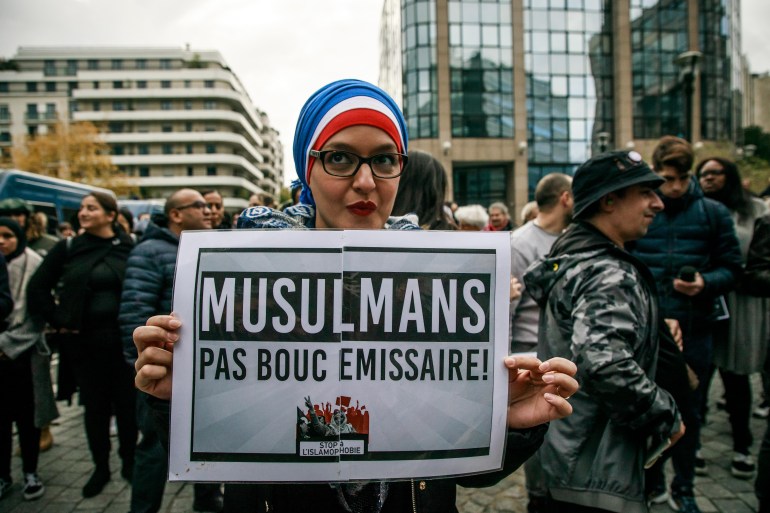 A woman wearing a tricolore veil holds a poster reading 'Muslims but not scapegoat' as protesters gather in front of Cnews TV headquarters to protest against the French polemist and writer Eric Zemmour in Boulogne, near Paris