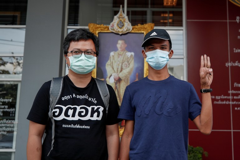 Pro-democracy protest leaders Anon Nampa (L) and Panupong 'Mike' Jadnok who is making the three-finger salute stand in front of an official portrait of Thailand's king