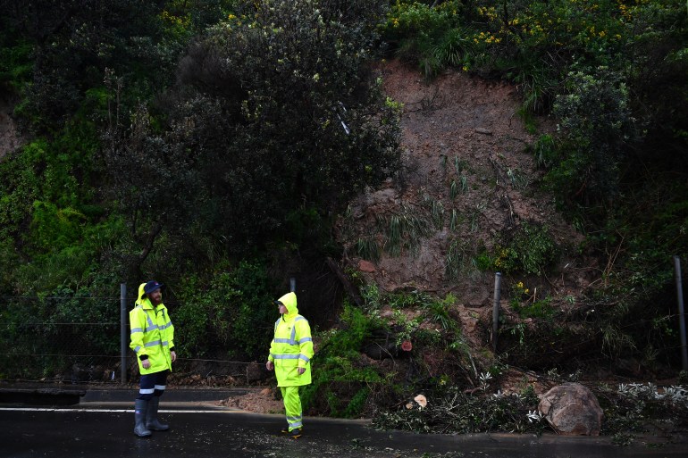 Emergency services in reflective suits patrol a road damaged by a landslide south of Sydney