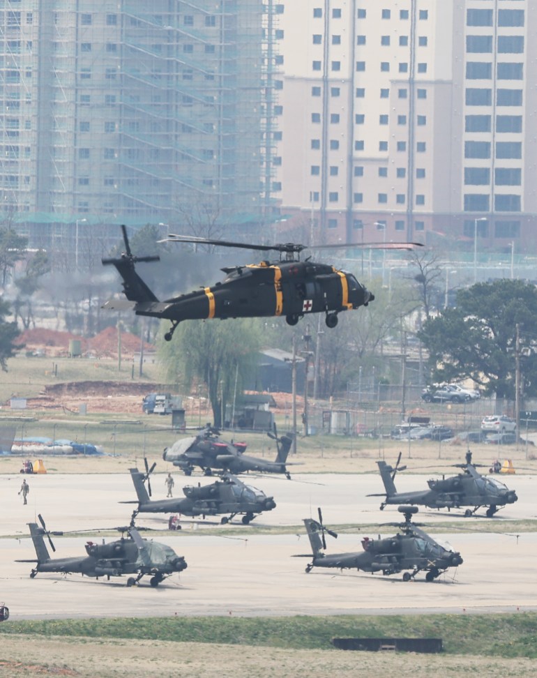 Military helicopters in the air and on the ground at US Army base Camp Humphreys with residential tower blocks behind