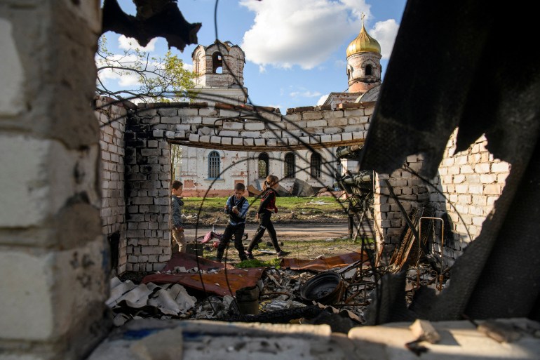 Local boys Faddei and Oleksandr play in front of a church damaged during Russia's invasion of Ukraine, in the village of Kolychivka, in Chernihiv region.