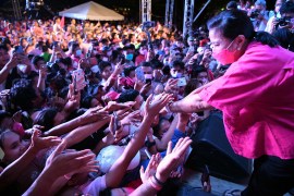 Leni Robredo in pink squats down to shake the outreached hands of supporters at a rally in eastern Samar in the Philippinesy in