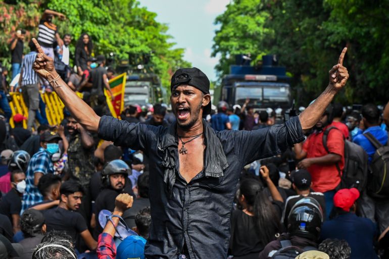 A university student in black shirt and bandana holds his arms out after being hit with water cannon in Colombo
