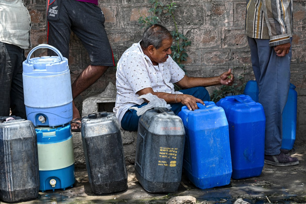 A man waiting to refill the containers with tap water supplied by the government on a hot summer day in Pali.