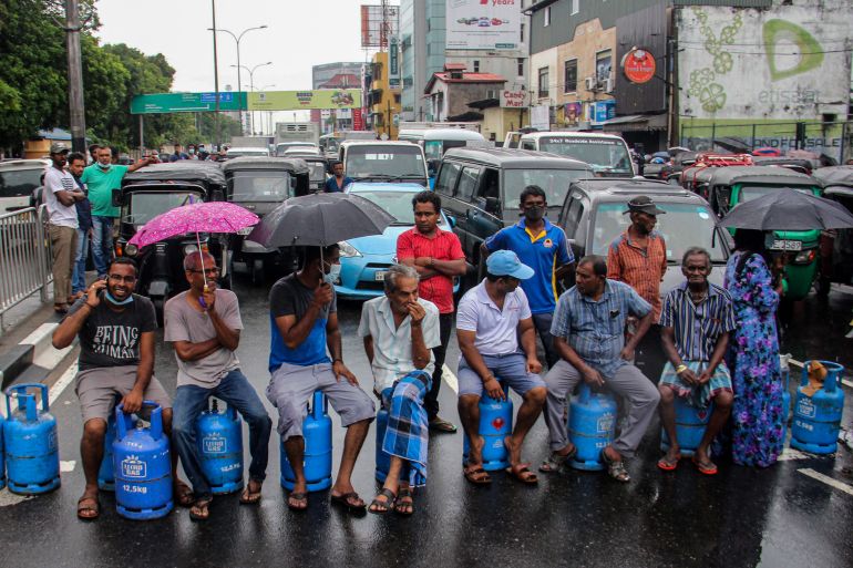 People sit on empty Liquified Gas Cylinders (LPG) as they block a road to protest against shortage of fuel and cooking gas in Colombo on May 13, 2022 [AFP]