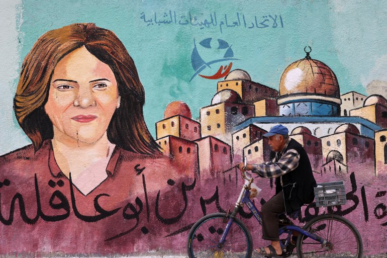 A Palestinian man rides his bicycle in front of a mural painted by an artist in honor of slain veteran Al-Jazeera journalist Shireen Abu Akleh, in Gaza City on May 13, 2022. - Abu Akleh, who was shot dead on May 11, 2022 While covering a raid in the Israeli-occupied West Bank, it was among Arab media's most prominent figures and widely hailed for her bravery and professionalism.