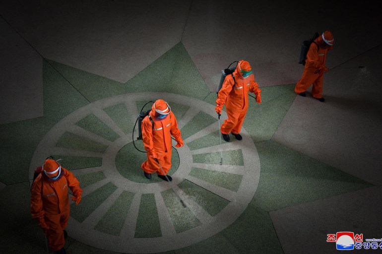 Three people in orange hazmat suits spray disinfectant at the railway station in Pyongyang
