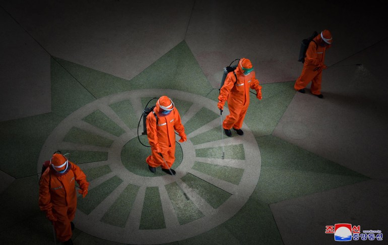 Three people in orange hazmat suits spray disinfectant at the railway station in Pyongyang 