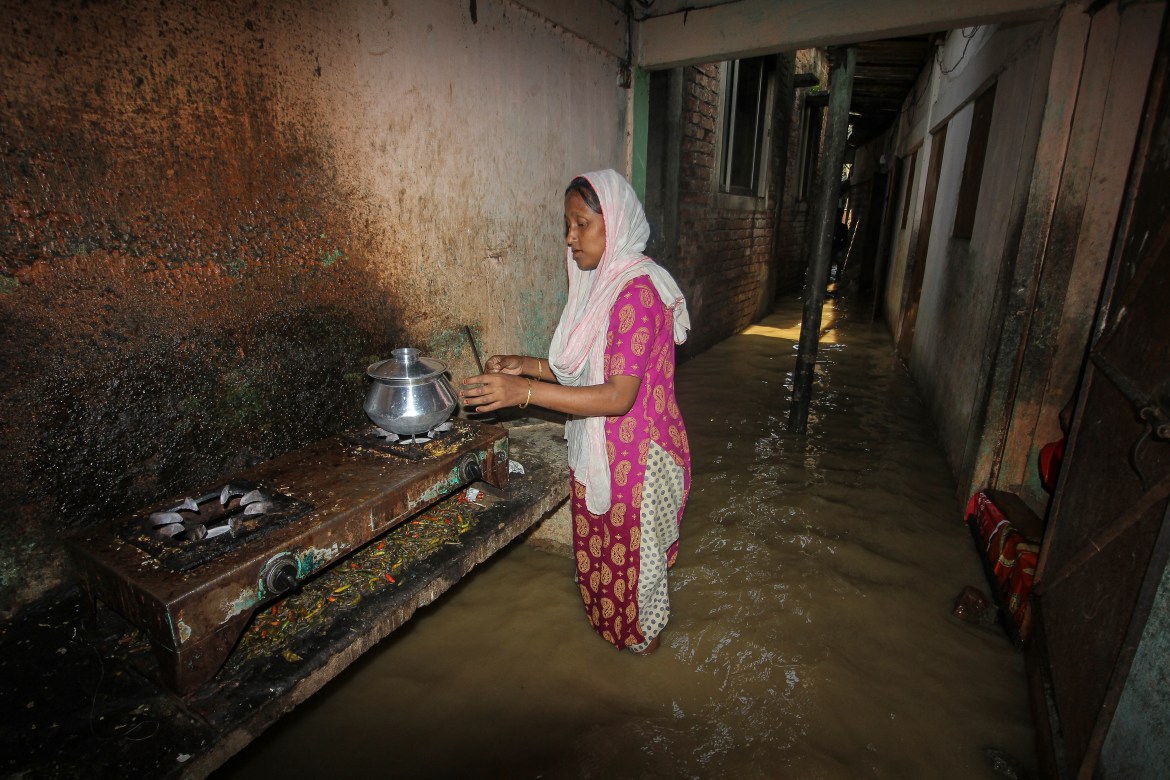 A woman cooks outside her home in a flooded corridor following heavy rainfalls in Sylhet