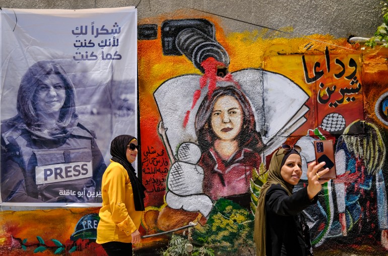 Palestinian women stand on May 19, 2022 in front of a mural, part of an art exhibit honouring slain Al-Jazeera journalist Shireen Abu Akleh