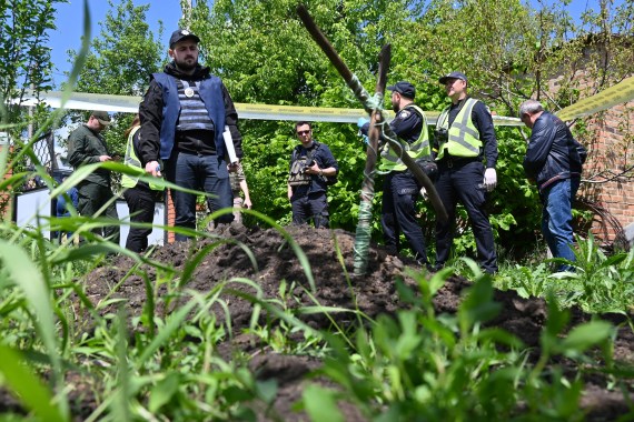 Local residents assist a Ukrainian police forensic team to exhume the body of a 51-year-old man allegedly shot dead on March 25, 2022 by a Russian soldier in the courtyard of his house, in the village of Mala Rogan, near Kharkiv