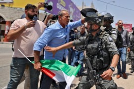 A confrontation between a man holding a Palestinian flag and Israeli border guards in the occupied West Bank town of Hauwara, on May 27, 2022 [Jaafar Ashtiyeh/AFP]