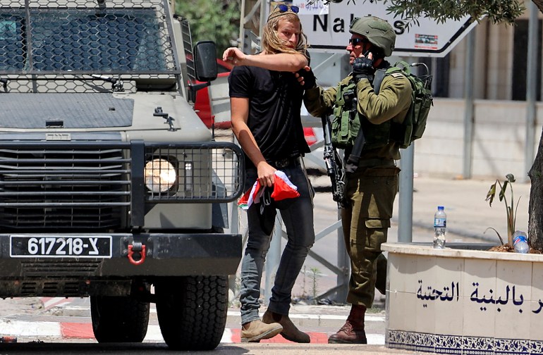A Jewish settler holds a Palestinian flag that he removed, as a member of the Israeli security forces tries to prevent him from doing so in the occupied West Bank town of Huwara, on May 27, 2022 [Jaafar Ashtiyeh/AFP]