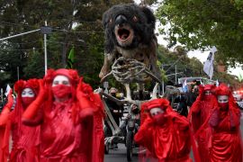 Activists in red cloaks and white masks carry a giant sculpture of a burning koala through Melbourne's streets during a climate protest