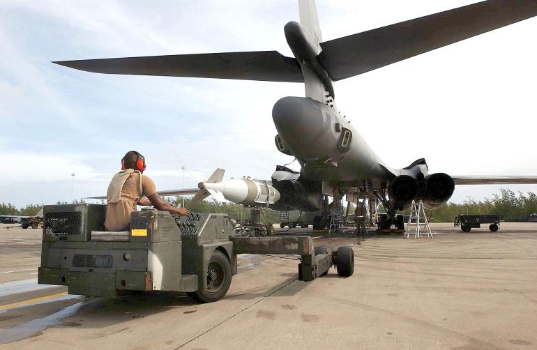 Военнослужащие ВВС США загружают бомбу в самолет на взлетно-посадочной полосе базы Диего-Гарсия.
