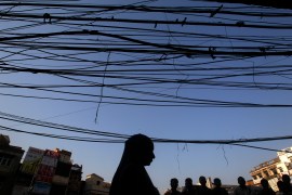 People are silhouetted against the backdrop of overhead wires and cables on a street in Delhi, India