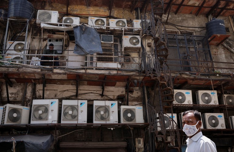 A man uses his mobile phone as he sits amidst the outer units of air conditioners, at the rear of a commercial building in New Delhi