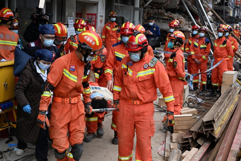 Rescue workers carry an injured person on a stretcher at a site where a building collapsed