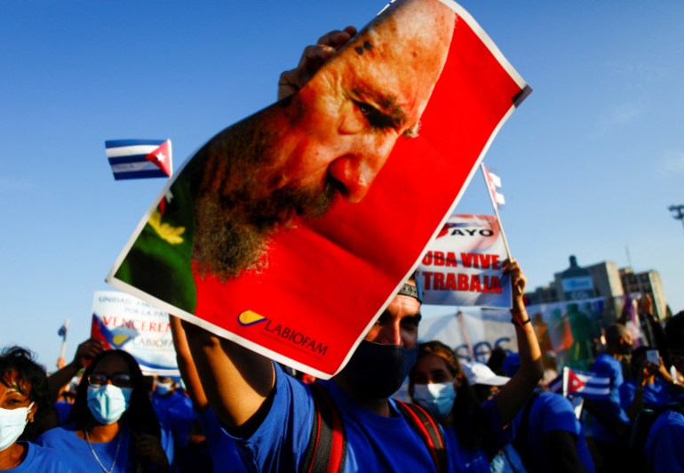 Un hombre sostiene una foto del difunto presidente cubano Fidel Castro mientras miles de personas marchan por la Plaza de la Revolución para conmemorar el Primero de Mayo, en La Habana, Cuba, el 1 de mayo de 2022. [Claudia Daut/Reuters]