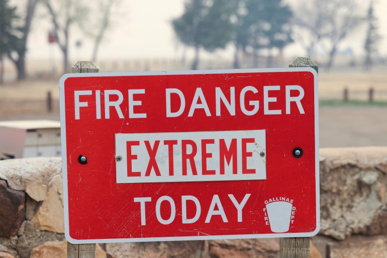 A red signboard warns of 'extreme' fire danger in New Mexico amid a charred landscape and smoke haze
