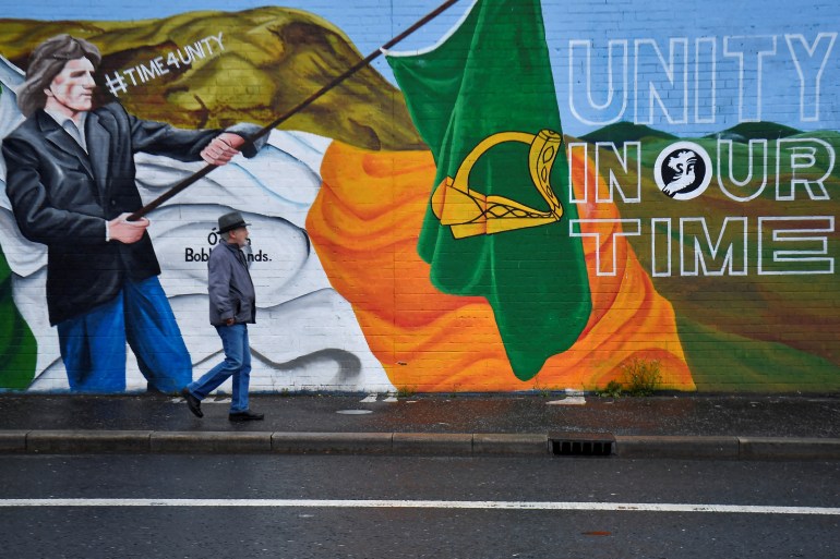 A man walks past a mural saying "Unity in our Time"