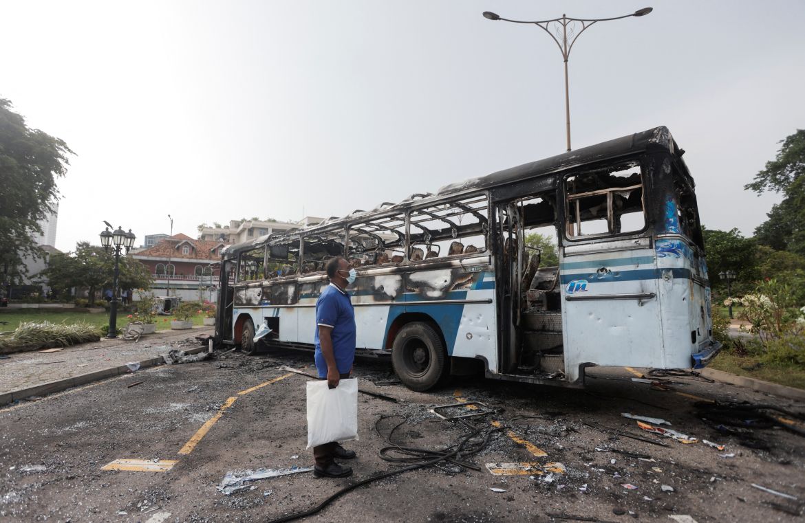 A man looks at a damaged bus of Sri Lanka's ruling party supporters after it was set on fire during a clash of pro and anti-government demonstrators near the Prime Minister's official residence