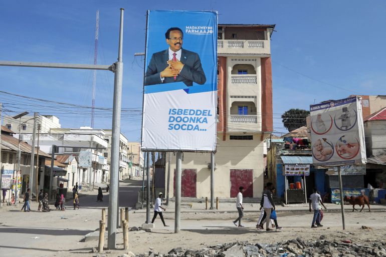 People walk past an election banner of incumbent Somali President Mohamed Abdullahi Mohamed in Mogadishu, Somalia