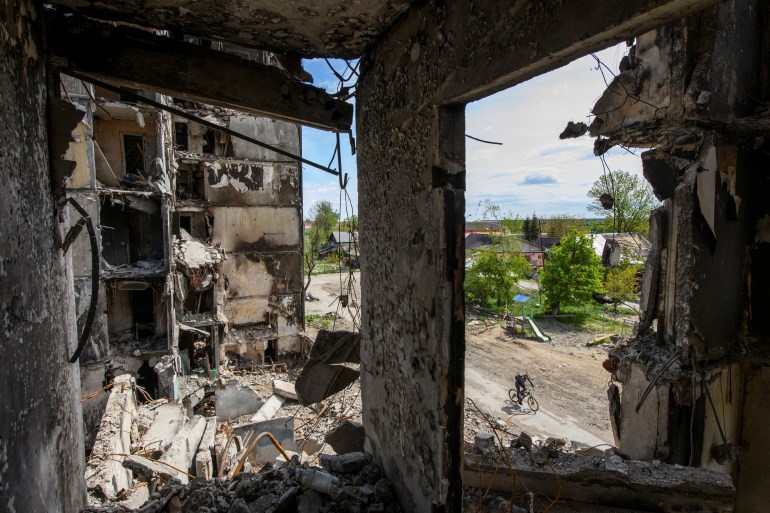 A resident rides a bicycle past a destroyed building in the Kyiv region