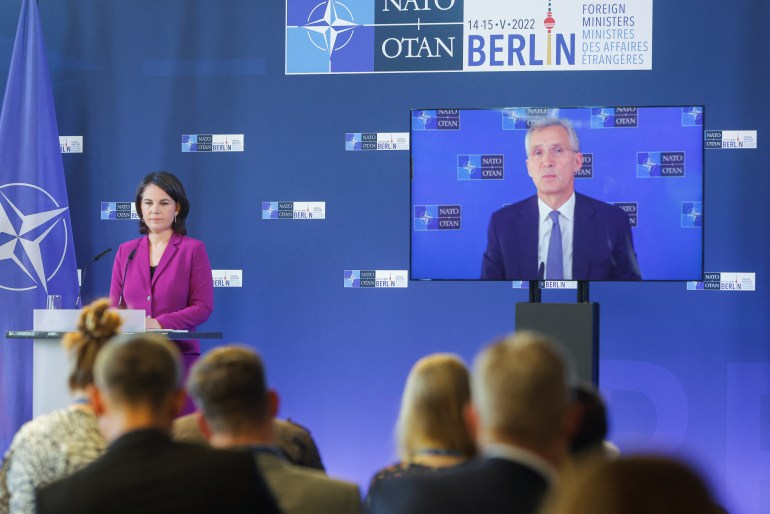 German foreign minister Annalena Baerbock stands next to NATO Secretary General Jens Stoltenberg, seen on a screen speaking during a news conference