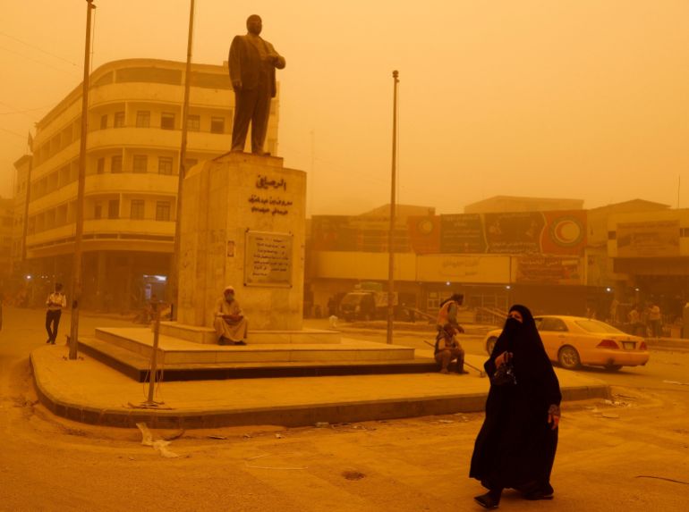 A woman walks past a statue of Iraqi poet Abdel Ghani Maarouf al Rusafi during a sandstorm in Baghdad,
