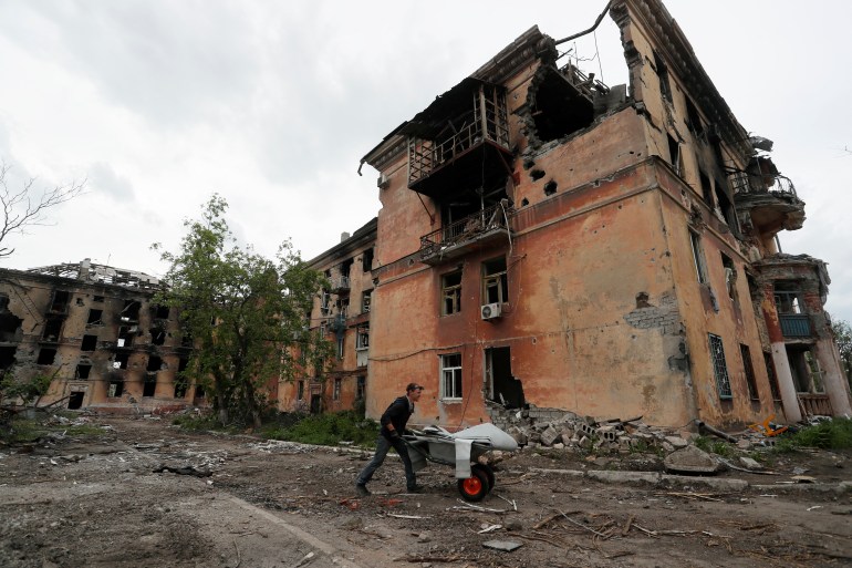 A local resident pushes a wheelbarrow past a heavily damaged apartment building