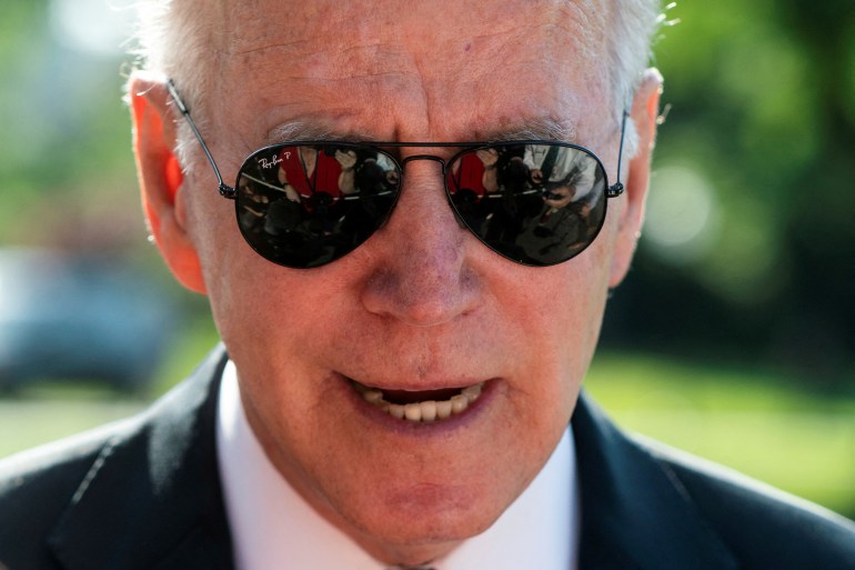 Wearing dark aviator sunglasses and a black suit President Joe Biden speaks to the media at the White House.