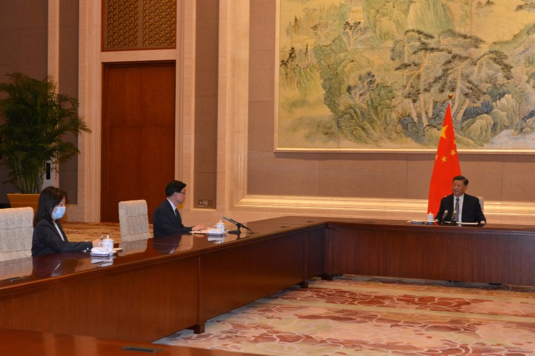 John Lee (at left) meets Xi Jinping (centre) around a massive table in a cavernous hall with a traditional Chinese painting on the wall and a Chinese flag hanging behind Xi's right shoulder
