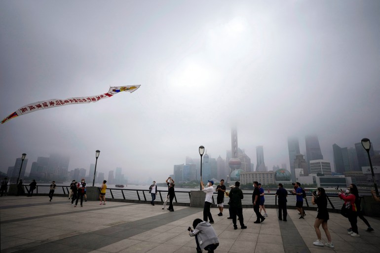 A man flies a kite as people walk on the Bund in Shanghai beneath grey skies on Wednesday morning