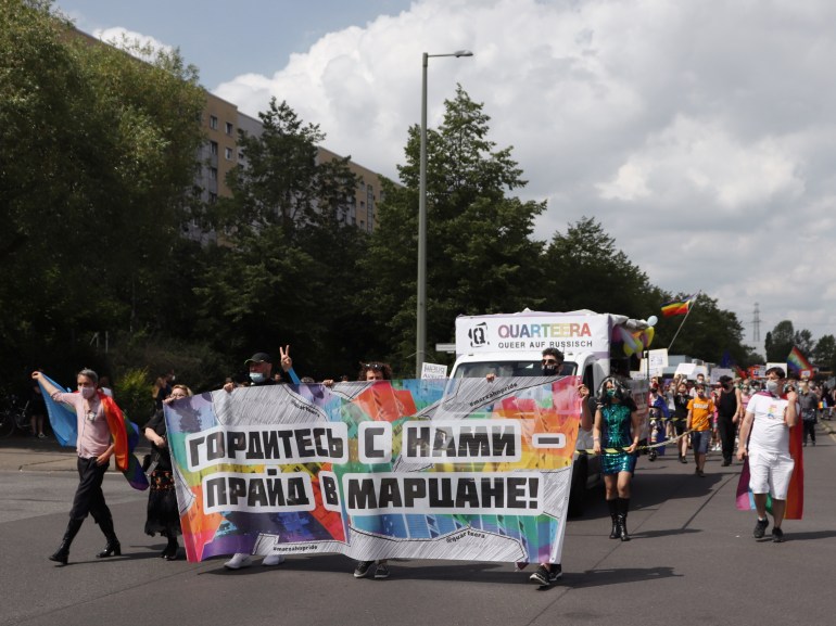 A photo of a large group of people walking through the street holding a large colourful poster with a sentence in Russian and a large group walking behind the poster with some holding a sign that says "Quarteera".