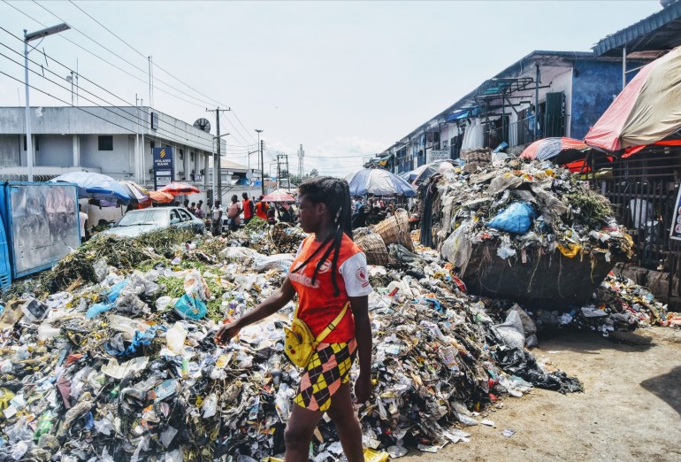 A woman walks beside the refuse dump at Watts Market