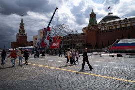 People walk in Red Square where municipal workers install decorations for the celebration of Victory Day in Moscow, Russia.