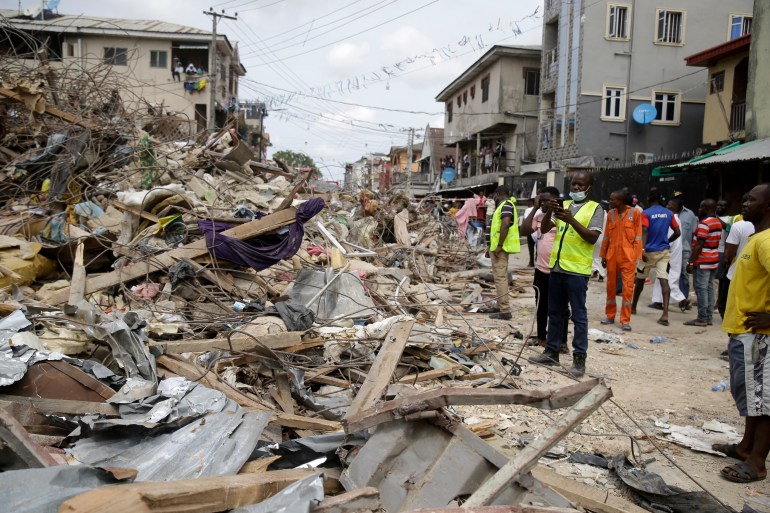 People stand by the site of a collapsed three-story building in Ebutte- Metta in Lagos, Nigeria