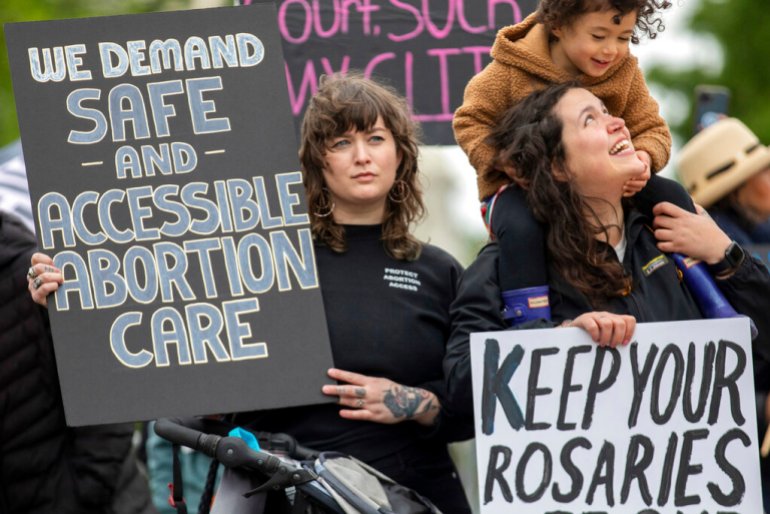 Abortion-rights protesters Holly Strandberg, left, and Kara Coulombe and her daughter Hana Uyehara, 3, hold signs during a demonstration outside of the U.S. Supreme Court in Washington, in May 2022. 