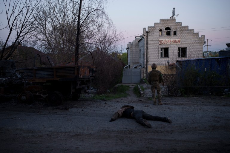 A Ukrainian serviceman is seen standing next to the body of a suspected Russian soldier in a village near Kharkiv